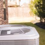 Modern air conditioning unit on a grass lawn beside a brick wall, showcasing SOS Heating & Cooling's HVAC services.