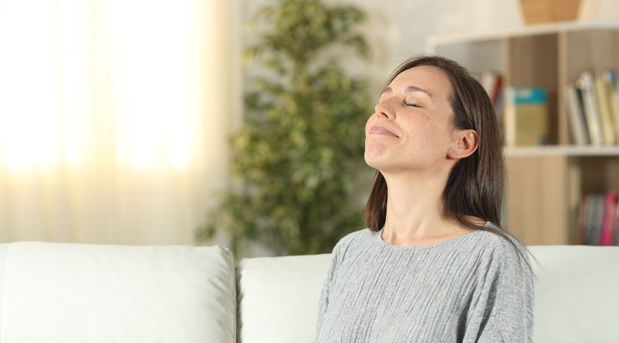 Calm woman meditating in a serene minimalist living room with a light sofa and indoor plants.